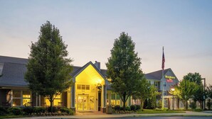 A hotel with a well-lit entrance, large windows, and a flagpole with an American flag.