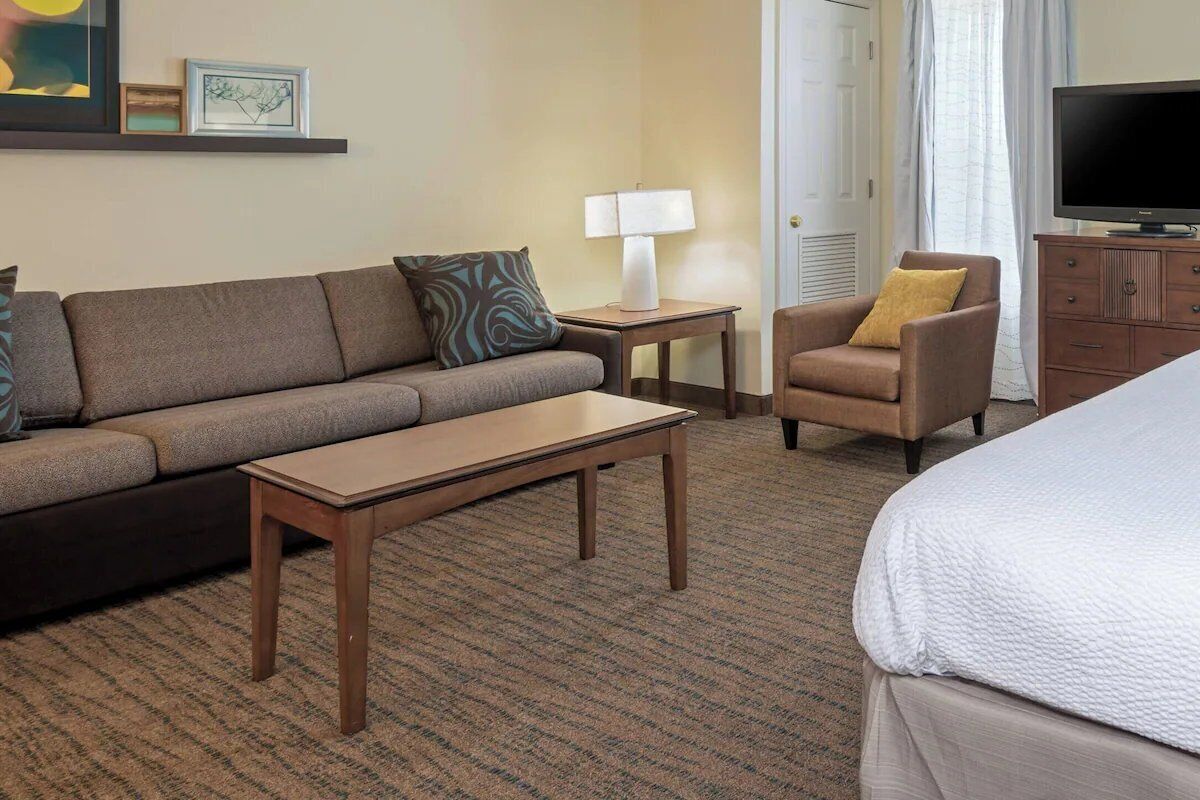 Ein Hotelzimmer mit einer Couch, einem kleinen Tisch, einem Sessel, einem Fernseher und einem Bett.