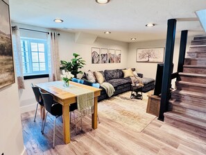 A living room with a sofa, a dining table, and a staircase. - Stunning, spotless two-bed basement suite in newly renovated duplex (Idaho Falls)