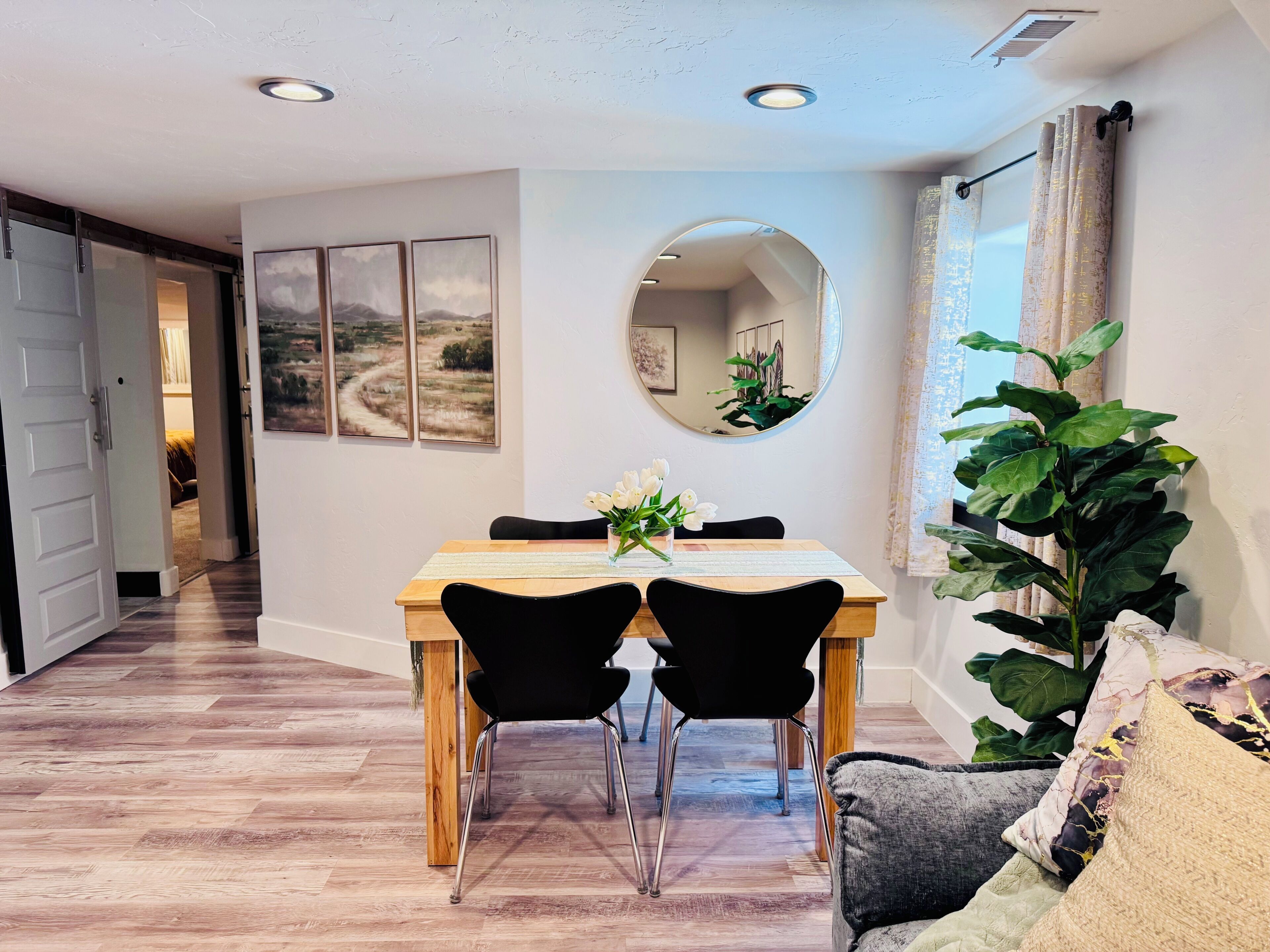 Un coin repas avec une table en bois, des chaises noires, un miroir et une plante en pot.