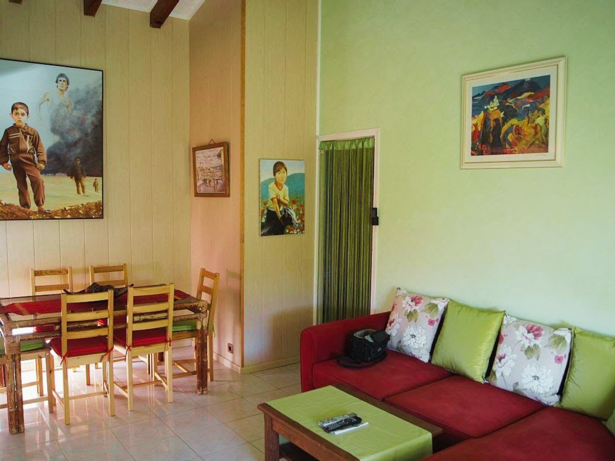 Una sala de estar con un sofá rojo, cojines verdes, una mesa de centro de madera y un cuadro en la pared.