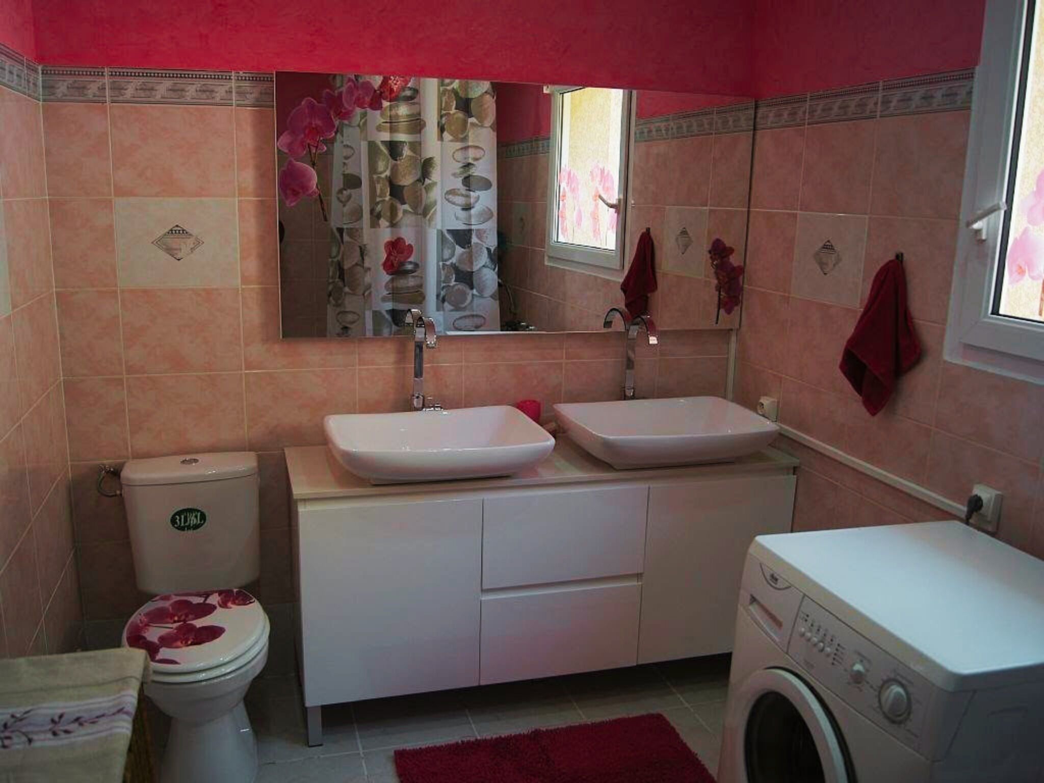 A bathroom with a toilet, two sinks, a mirror, and a washing machine.