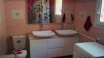 A bathroom with a toilet, two sinks, a mirror, and a washing machine.
