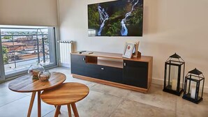 A modern living room with a large TV, a wooden dining table, a black and wooden entertainment unit, and a view through a large window. - Dpto muy buena ubicacion en Salta, Capital (Salta)