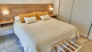 A neatly made bed with white and mustard pillows, wooden headboard, bedside lamps, and a wooden ladder. - Dpto muy buena ubicacion en Salta, Capital (Salta)