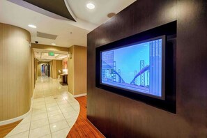 Un pasillo de hotel con una pared curva, un televisor montado mostrando una obra en construcción y una señal de salida.