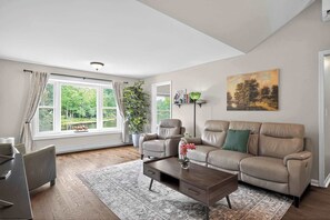 A modern living room with a sofa, coffee table, and a view of greenery outside.