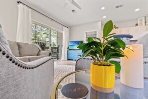 A living room with a sofa, a coffee table with a plant, and a TV in the background. - Unique Treehouse Getaway in Sea Trail - Sunset Beach (Sunset Beach)
