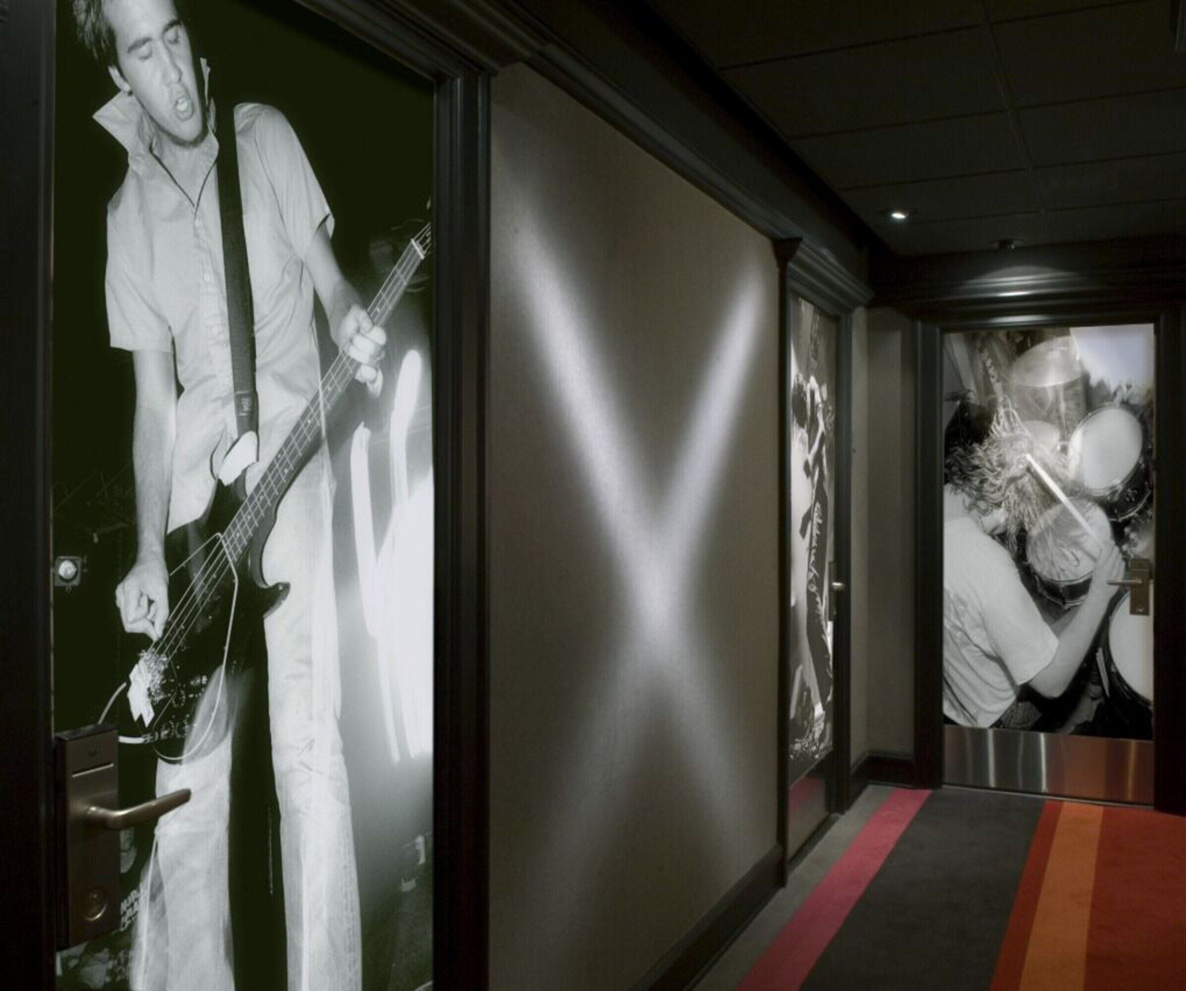 Un couloir avec une grande affiche représentant un musicien, une porte dotée d’une poignée et un tapis rouge.