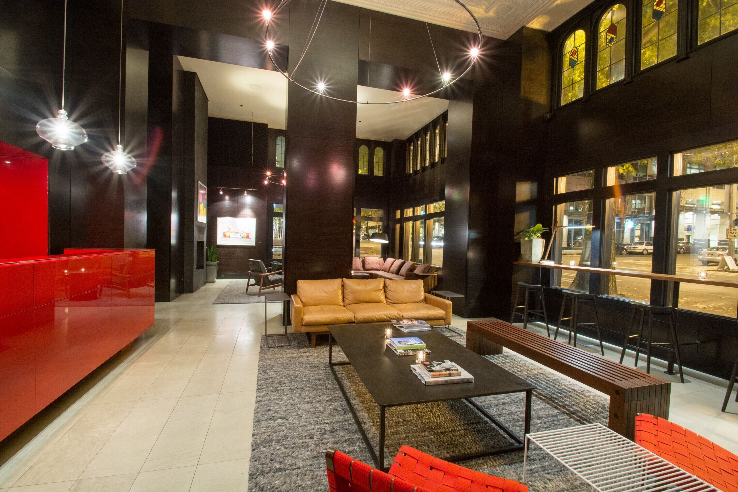 A modern lobby with a red reception desk, a leather sofa, a coffee table, and a view of the street through large windows.