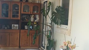 A room with a wooden ceiling, a white table with a vase of flowers, a wooden cabinet with glass doors, and a window with a picture frame. - Ti Zaquiel Farm (Porto de Mós)
