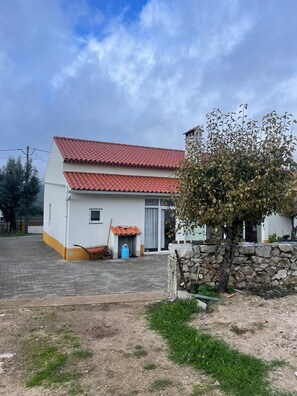 A two-story building with a red-tiled roof, a small porch, and a stone wall.