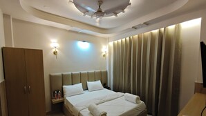 Habitación de hotel con cama, armario, mesita de noche, apliques, cortinas y ventilador de techo.