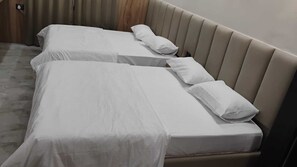 Habitación de hotel con dos camas, cada una cubierta con sábanas blancas y almohadas, y cabeceros de madera.