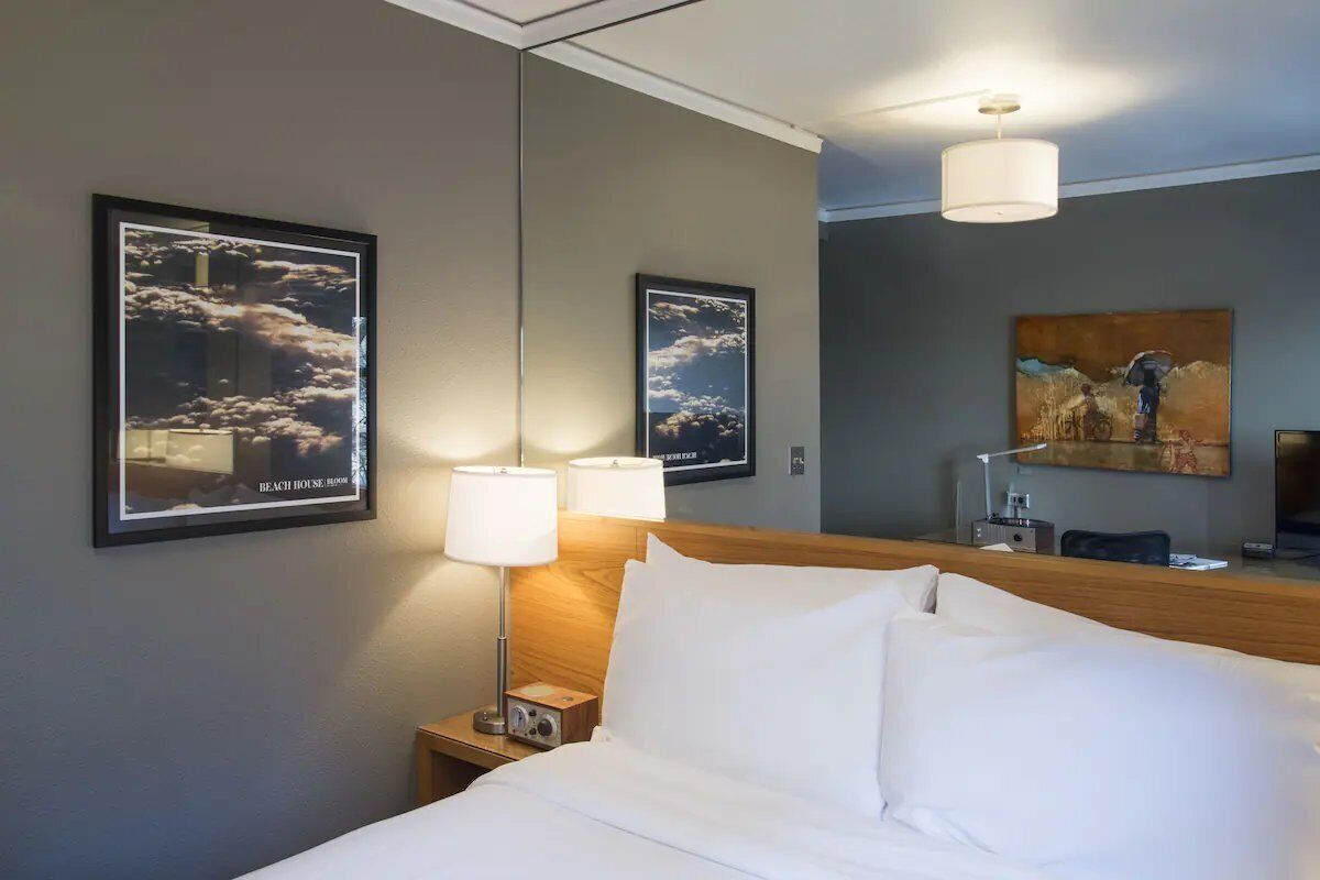 Een hotelkamer met een bed, twee wandlampen, een bureau met stoel, en twee ingelijste foto's aan de muur.