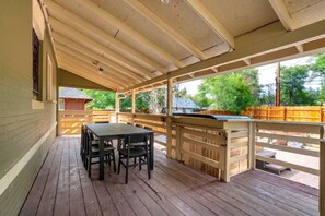 Un porche techado con mesa y sillas, barandas de madera y vistas del entorno.