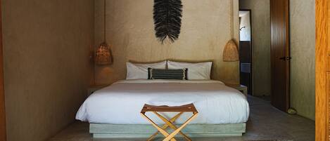 A bedroom with a bed, a woven chair, a hanging feather decoration, and two wall-mounted lamps.
