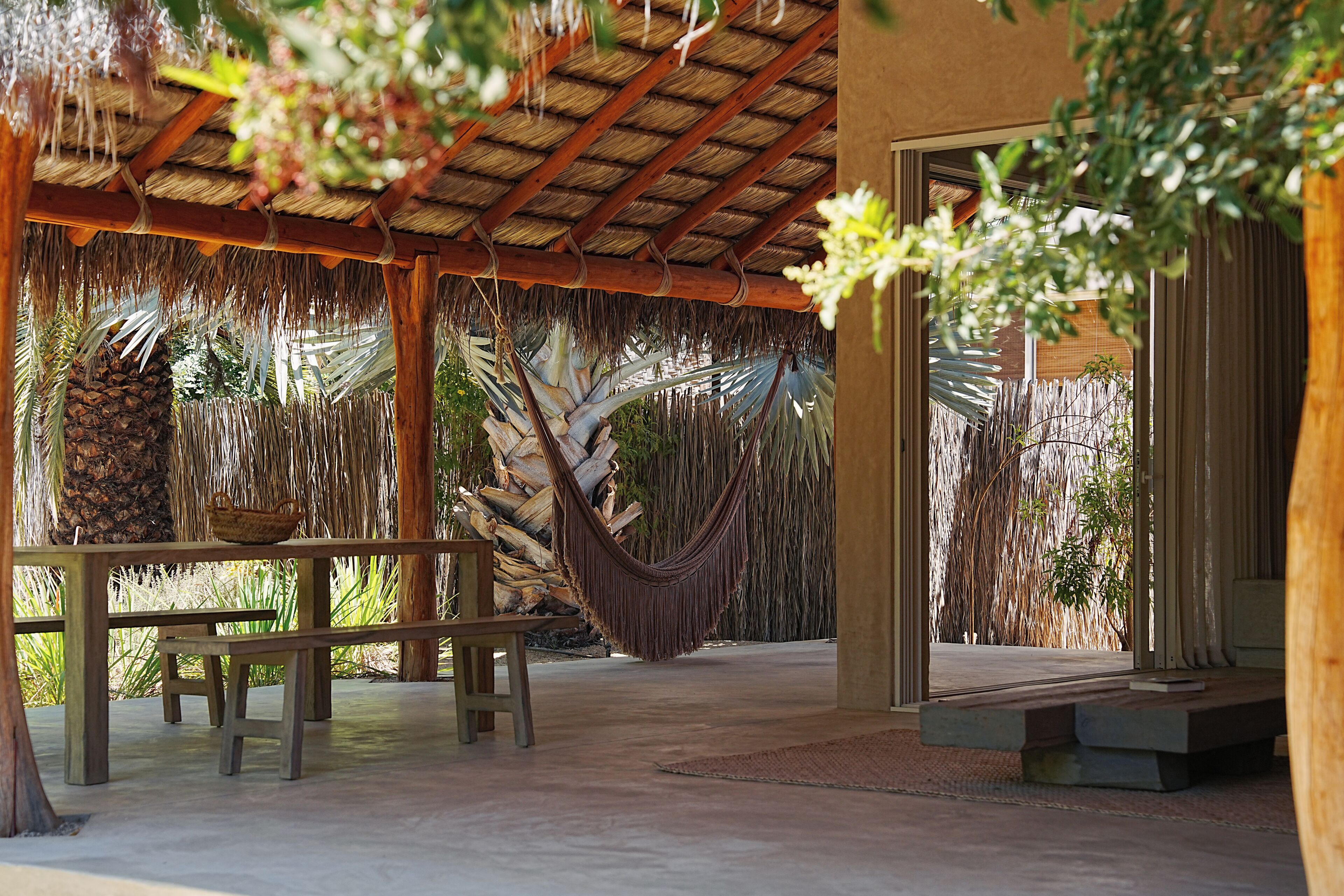 A covered outdoor area with a hammock, wooden benches, and a table with a basket.