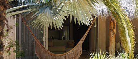 Una hamaca bajo una palmera, una puerta corrediza de vidrio y un sofá dentro de una habitación.