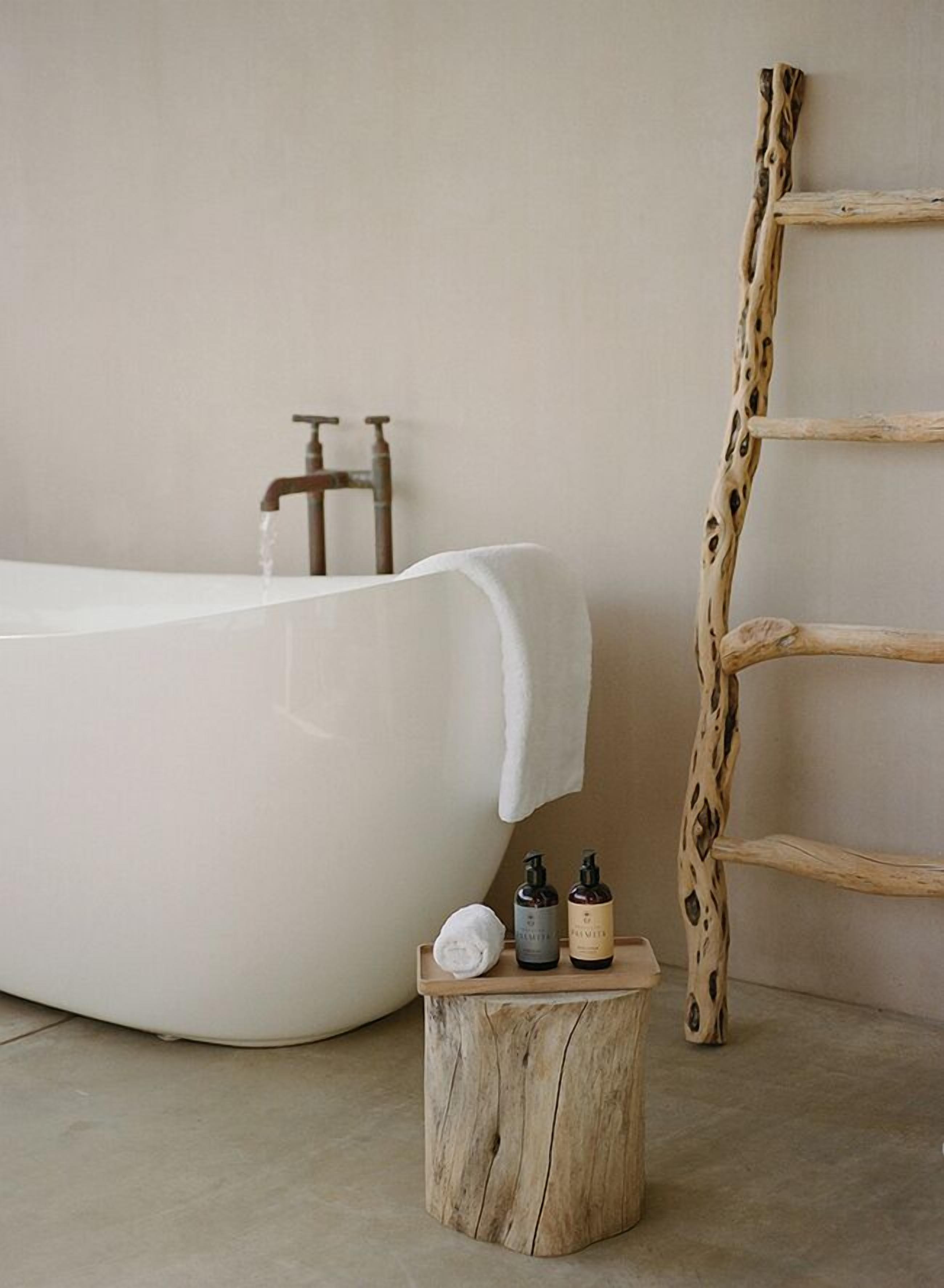 A bathtub with a wooden ladder, a wooden stool with toiletries, and a white towel.