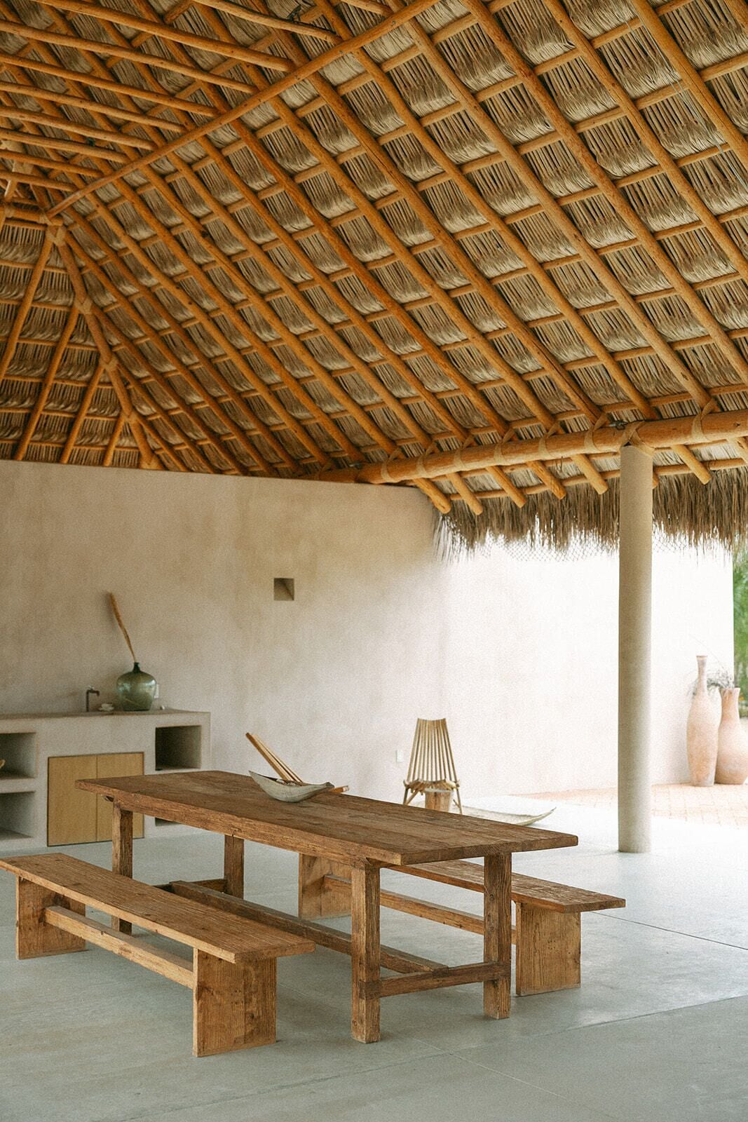 A spacious room with a thatched roof, a wooden table, a bench, and a chair.