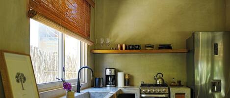A kitchen with a stainless steel refrigerator, a stove, a coffee maker, and a window with blinds.