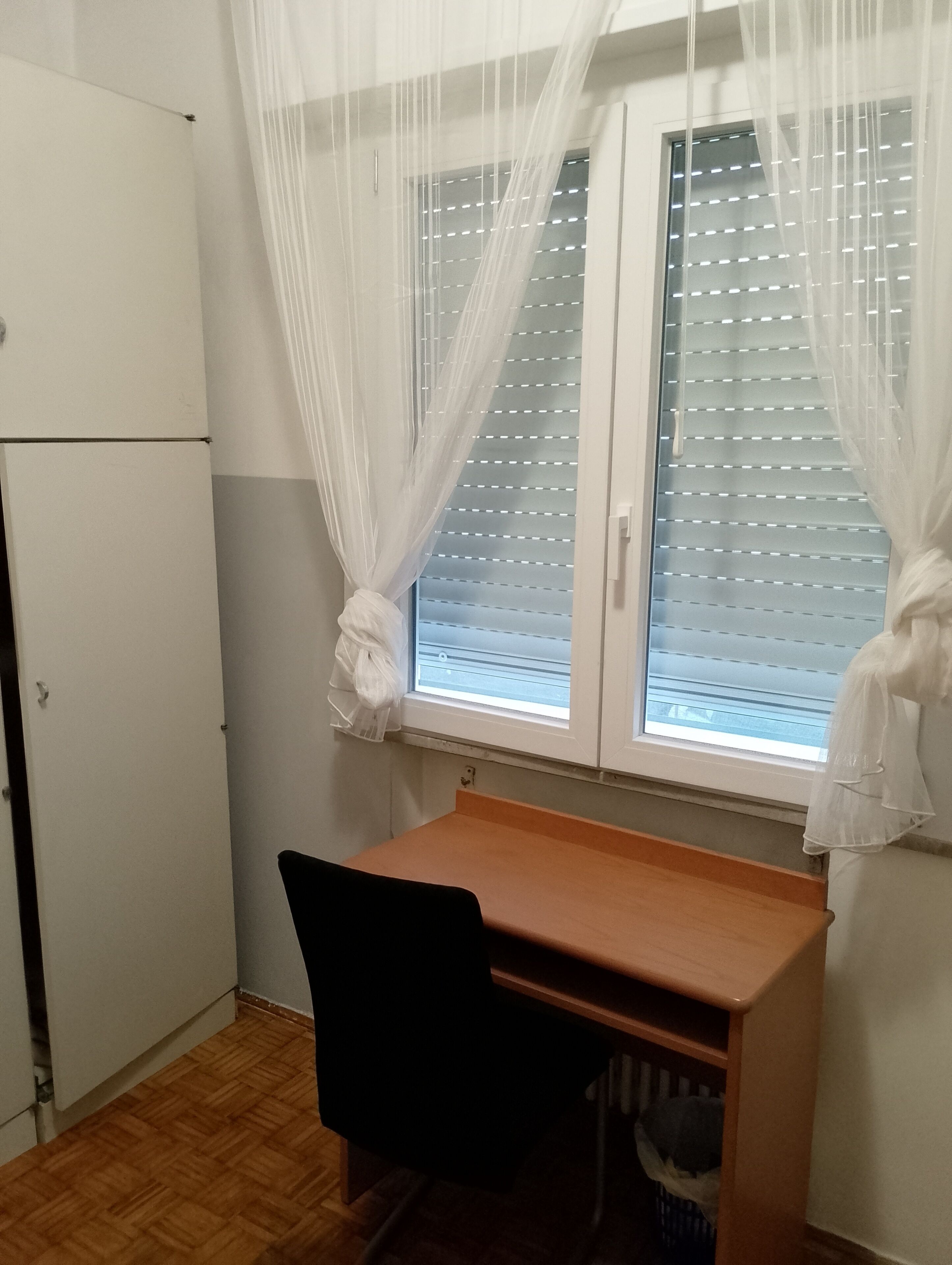A small room with a desk, chair, and a window with blinds.