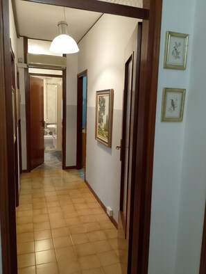 Ein Korridor mit Fliesenboden, einer Pendelleuchte und gerahmten Bildern an der Wand.
