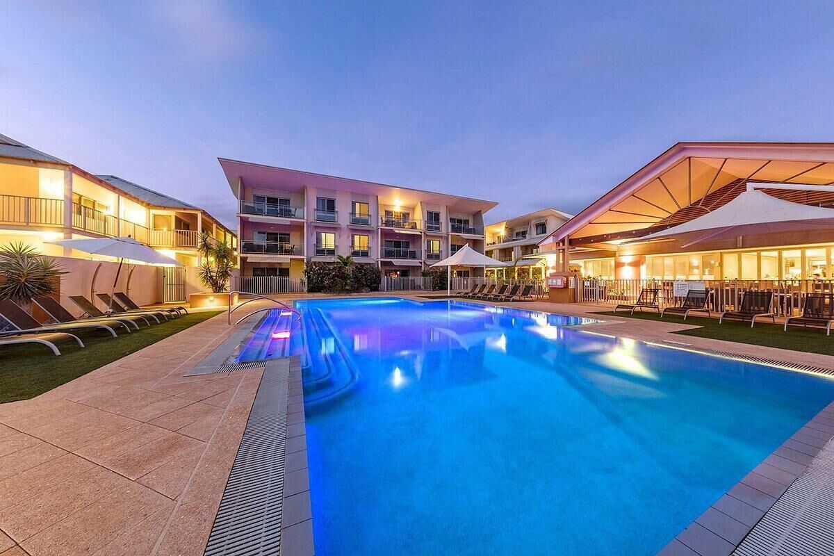 Evening view of the illuminated pool with mosaic tile steps and surrounding beige deck and loungers.