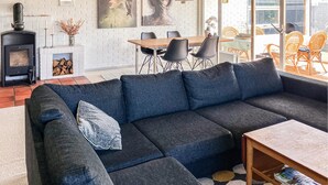 Un salon moderne avec un canapé bleu foncé, une cheminée, un coin repas avec des chaises et une grande fenêtre.