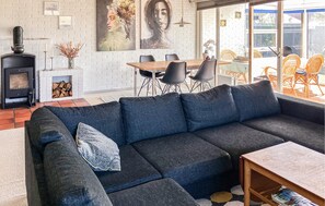A modern living room with a dark blue sofa, a fireplace, a dining area with chairs, and a large window.