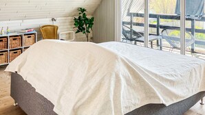 Une chambre à coucher avec un lit, une fenêtre, une plante et une vue sur l’extérieur.