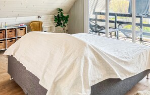 Ein Schlafzimmer mit Bett, Fenster, Pflanze und Ausblick nach draußen.