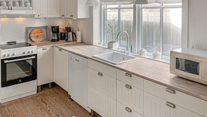 Una cocina moderna con muebles blancos, horno empotrado, lavavajillas, fregadero y ventana con vistas al exterior.
