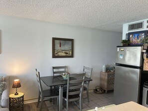 Ein Essbereich mit Tisch, Stühlen, einer Lampe, einem Bild an der Wand und einem Kühlschrank.