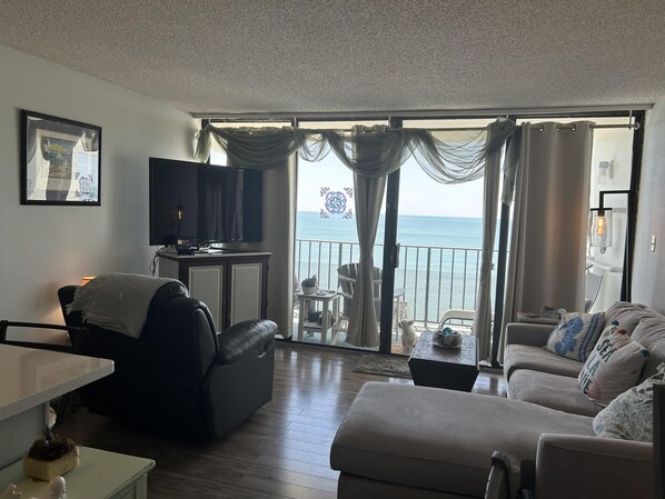 Ein Wohnzimmer mit Fernseher, einer Couch, einem Esstisch und einem Balkon mit Meerblick.