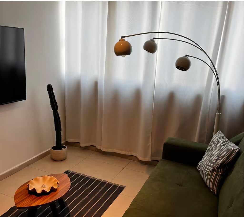 Een woonkamer met een groene bank, een houten salontafel, een vloerlamp en een cactus in een pot.