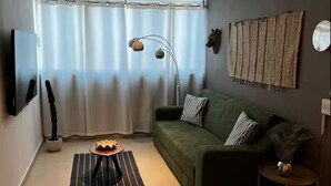 Uma sala de estar moderna com um sofá verde, um abajur, uma mesinha lateral e uma TV fixada na parede.
