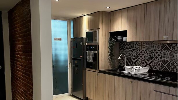 Cozinha moderna com armários de madeira, geladeira de aço inoxidável e bancada preta.
