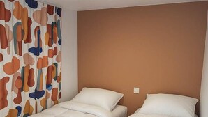 A hotel room with two beds, a plain brown headboard, and a colorful abstract curtain. - Mobile home with 4 bedrooms for 8 people (Sainte-Marie-la-Mer)
