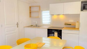 A modern kitchen with white cabinets, a central island, yellow chairs, and a hanging pendant light. - Mobile home with 4 bedrooms for 8 people (Sainte-Marie-la-Mer)