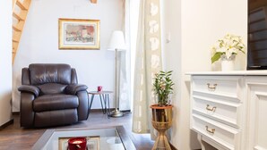 Una sala de estar con un sofá de cuero, una mesita redonda con una taza roja, una lámpara de pie, una planta en maceta y un aparador blanco con tiradores dorados.