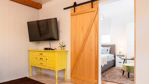 Una habitación con puerta corredera, televisor en la pared, cómoda amarilla y cama con colcha estampada.
