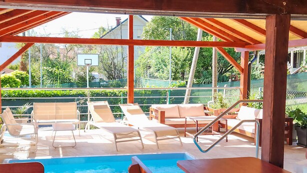 Un área de piscina al aire libre con sillones de descanso, una mesa de madera y un aro de baloncesto.