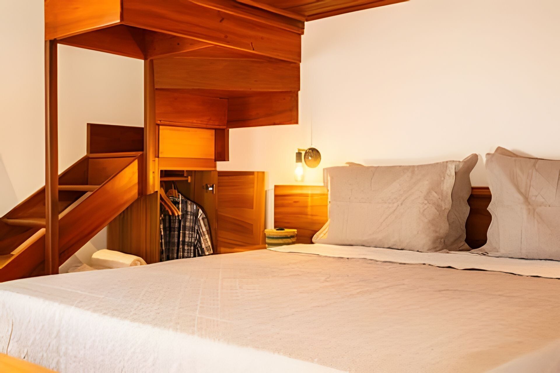 Ein Schlafzimmer mit einem Bett, einem Nachttisch, einer Lampe und einer Holztreppe.