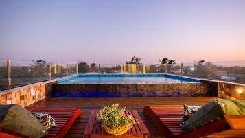 Ein Pool auf dem Dach mit Holzterrasse, Liegestühlen und einem Tisch mit Pflanze.
