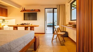 A modern hotel room with a bed, a dining table, a TV, and a view of the outside. - ARARA HOUSE  (Jijoca de Jericoacoara)