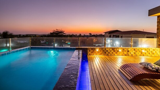 A swimming pool with a wooden deck and glass railing, surrounded by a sunset view. - ARARA HOUSE  (Jijoca de Jericoacoara)