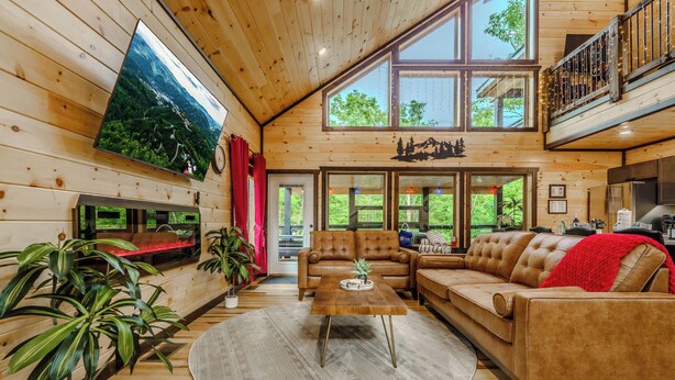 Ein großzügiges Wohnzimmer mit einem großen Flachbildfernseher, Ledersofas, einem Couchtisch und einem großen Fenster mit Blick auf Grünflächen.