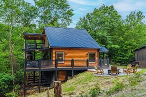 A cabin with a balcony, outdoor seating, and a view of the surrounding forest. - New Build 2B-2B Cabin With Hot Tub & Sauna (Sevierville)